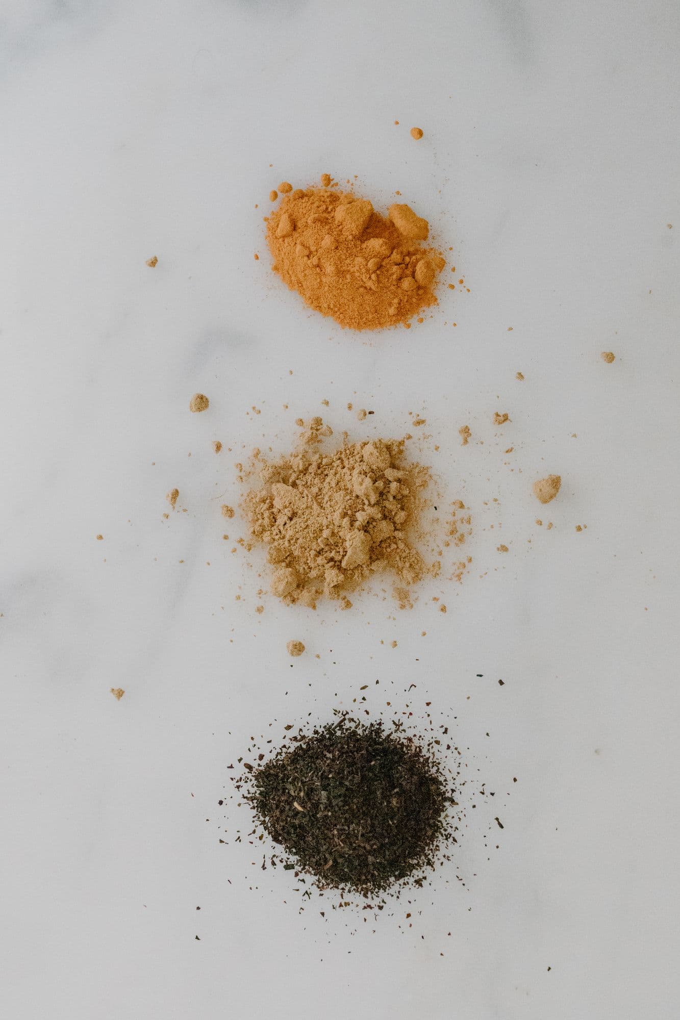 Ground turmeric, ginger and a dried herb laid out on white marble